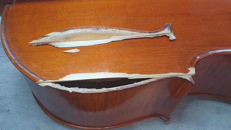 Fisură lungă și lemn crăpat pe placa de brad a unui violoncel, înainte de reparație